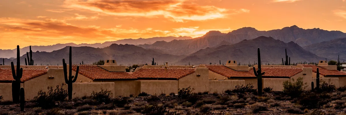 Desert mountains behind stucco rooftops at sunset with saguaro silhouettes